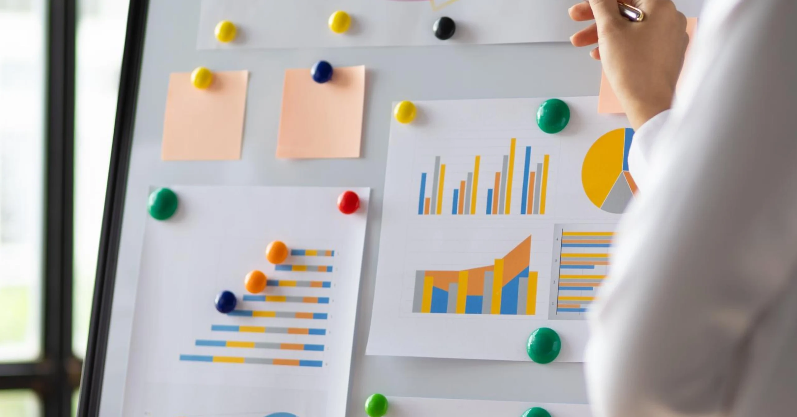 Business charts on bulletin board analyzed by a person, illustrating data trends with colorful graphs and sticky notes.