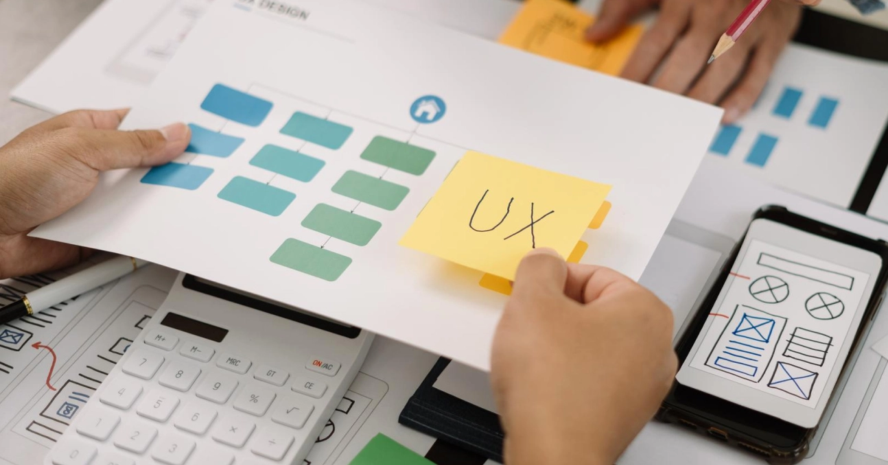 Person analyzing UX design with flowchart and mobile app wireframe on desk.