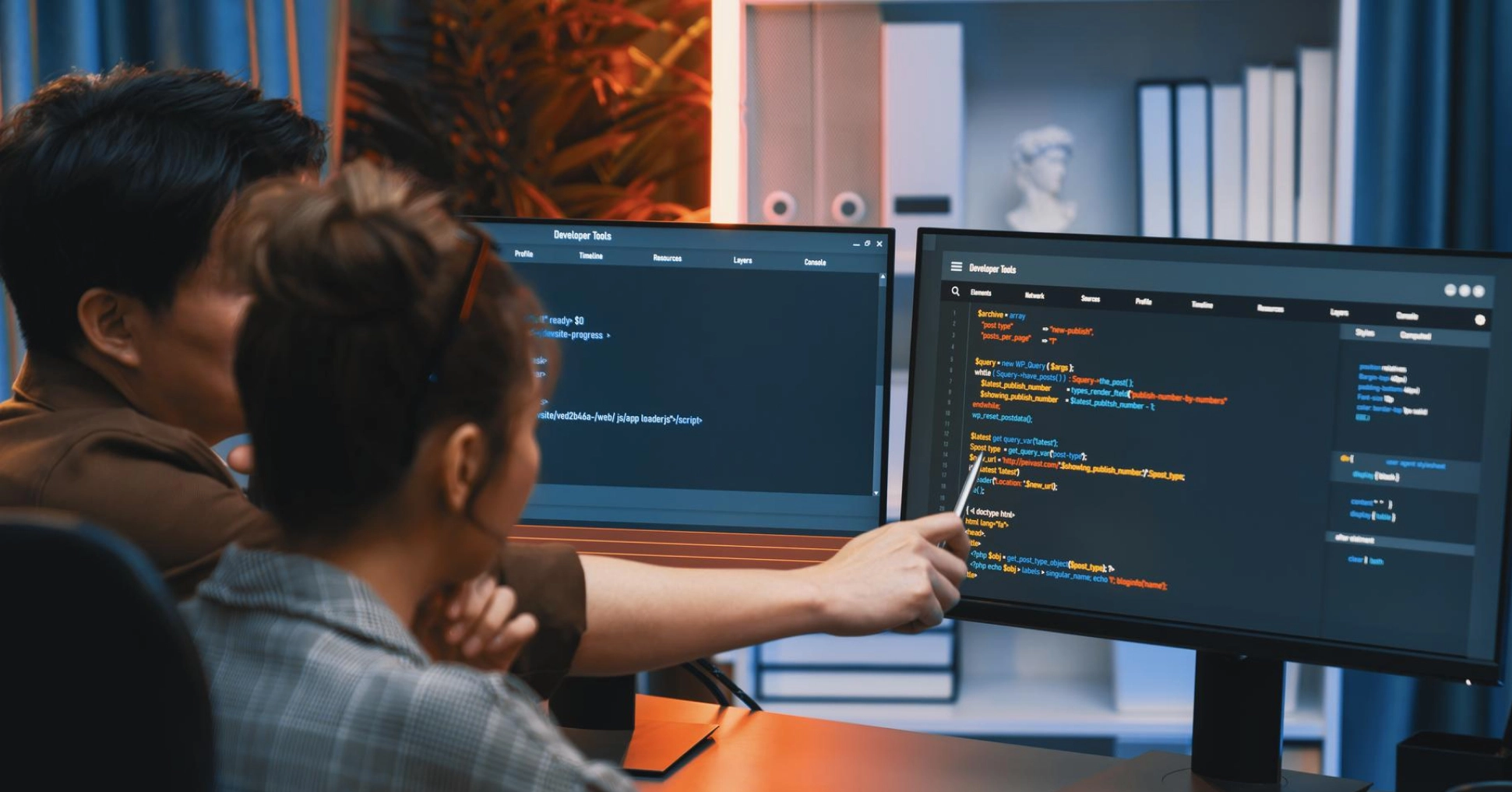 Developers collaborating on code, analyzing scripts on dual monitors in a modern office setting.