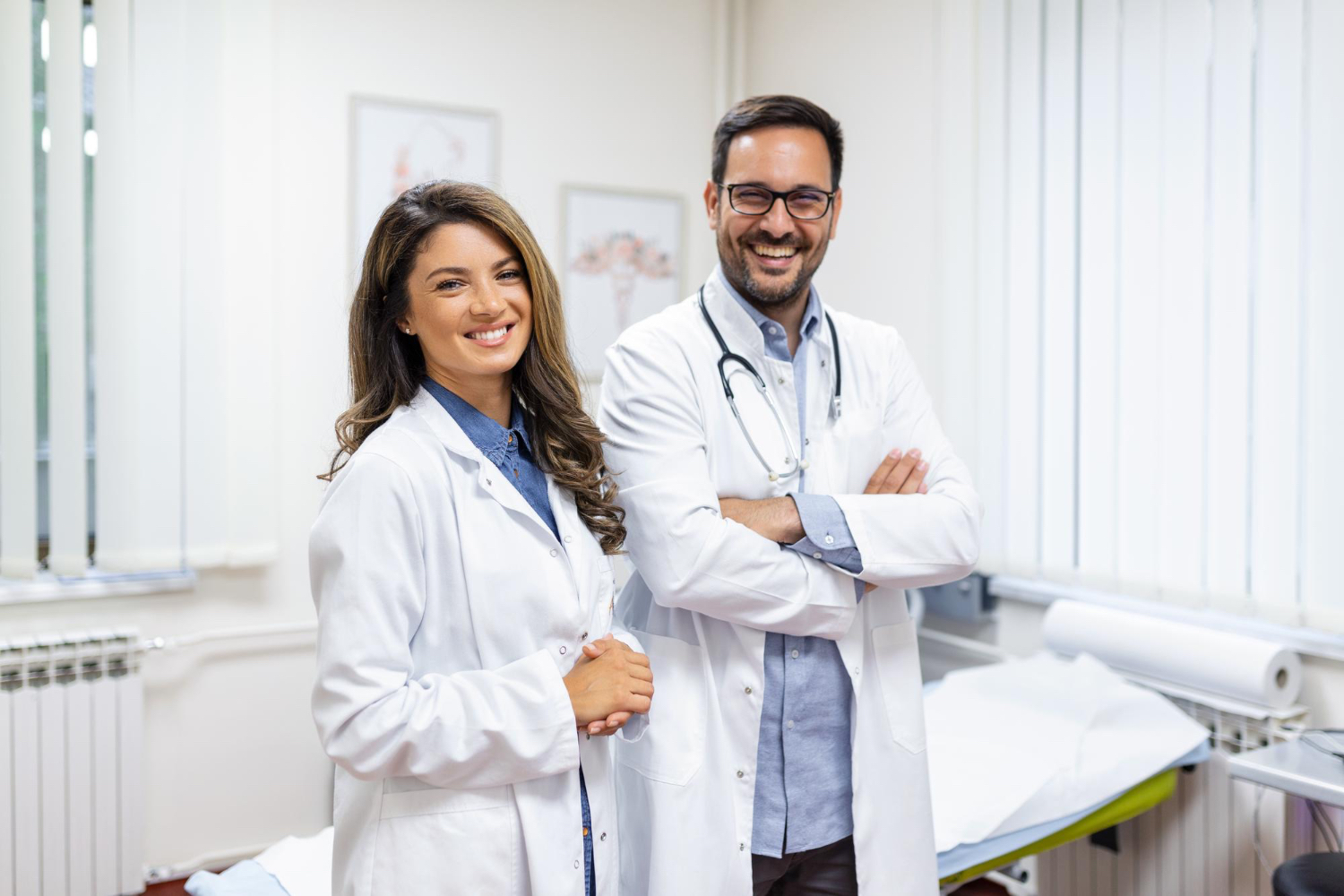 Two smiling doctors in a medical office, wearing white coats and stethoscope.