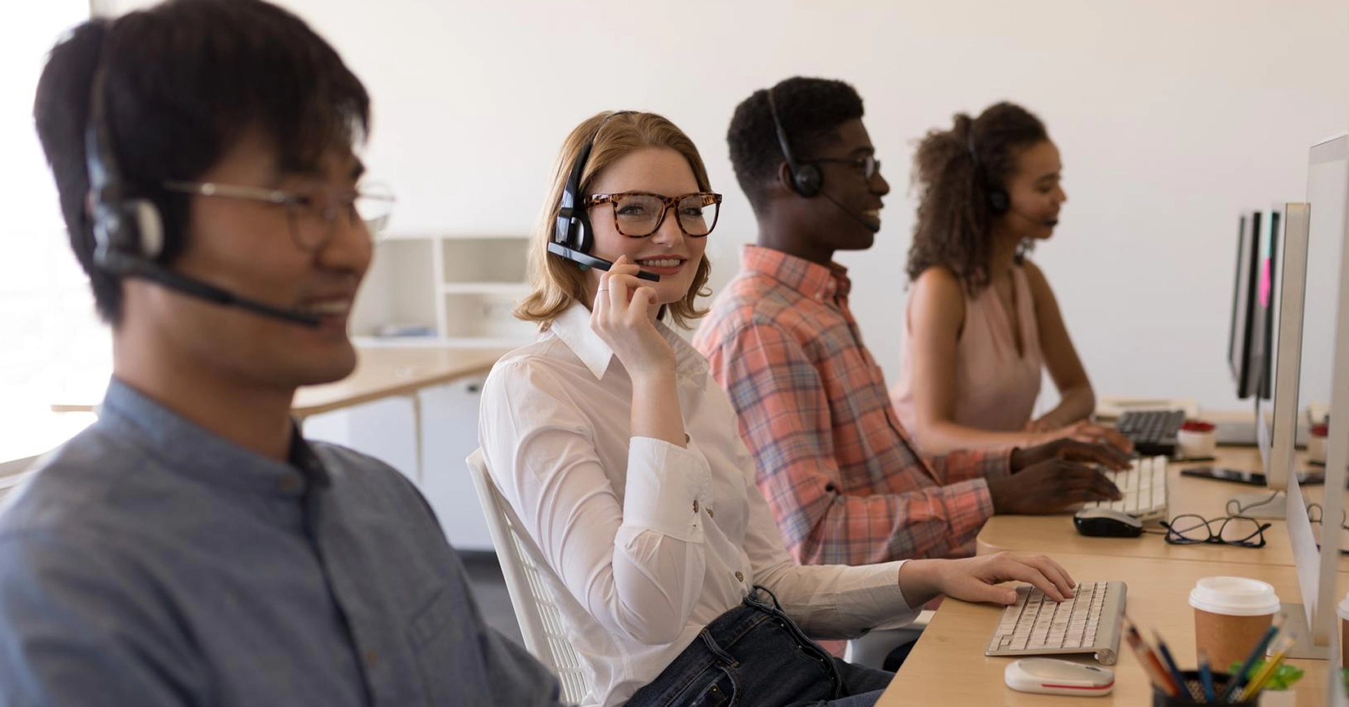 Smiling customer support team with headsets working at computers in modern office.